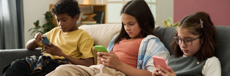 Crianças sentadas no sofá olhando para celulares, ilustrando a hiperconectividade e seus efeitos na saúde mental.