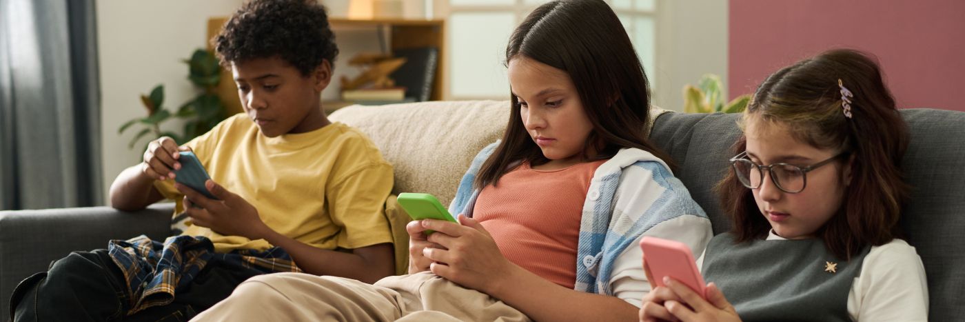 Crianças sentadas no sofá olhando para celulares, ilustrando a hiperconectividade e seus efeitos na saúde mental.